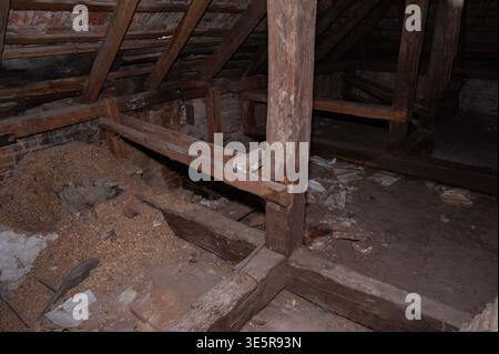 Ancienne structure de poutres en bois à l'intérieur de Dim Attic avec des murs de briques et des débris dispersés montrant des textures rustiques et la décomposition historique en basse lumière Banque D'Images
