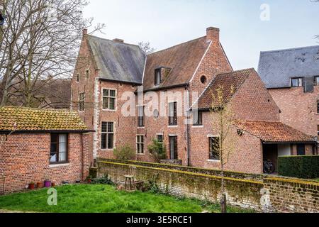 Vue pittoresque sur les maisons historiques en briques rouges dans le Groot Begijnhof, Louvain. L'image présente une pelouse verte luxuriante, des murs en pierre moussue et traditionnelle Banque D'Images