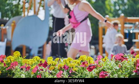 Journée d'été lumineuse à une aire de jeux avec des enfants flous jouant et des fleurs colorées Banque D'Images