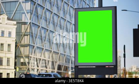 Panneau d'affichage vierge avec écran vert pour maquette sur une rue de la ville avec une architecture moderne en arrière-plan Banque D'Images