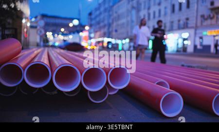 Nouveaux tuyaux en plastique rouge couchés sur une rue urbaine pendant la soirée pour les travaux d'infrastructure de la ville Banque D'Images