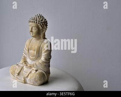 Cliché minimaliste et de haute qualité d'une statue de Bouddha assise dans une pose méditative. L'image doit présenter une texture altérée semblable à une pierre avec w Banque D'Images