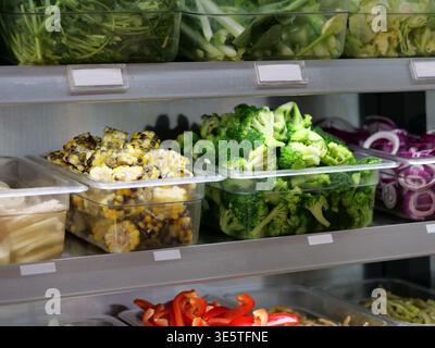 Un plan rapproché moyen et à grand angle comprend un buffet de salades réfrigérées ou un buffet avec des légumes frais hachés. Les récipients en plastique transparent sont Banque D'Images