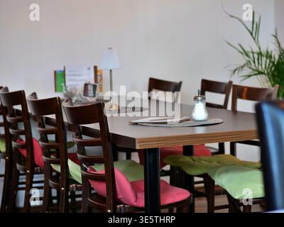 Une table à manger en bois confortable dans un café ou un restaurant lumineux. La table est entourée de chaises en bois sombre agrémentées de rose vif et de citron vert Banque D'Images