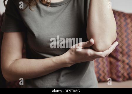 Femme assise sur un canapé à la maison et souffrant de douleurs au coude, de main massante, de blessures corporelles Banque D'Images