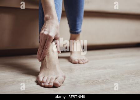 Femme assise sur un canapé à la maison et souffrant de douleurs aux jambes, de massage de la cheville, de blessures corporelles Banque D'Images