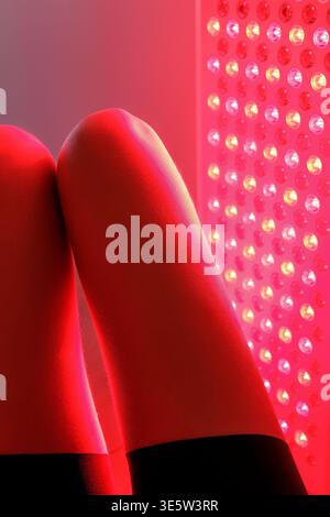 Femme faisant une thérapie de lumière rouge sur sa jambe inférieure Banque D'Images