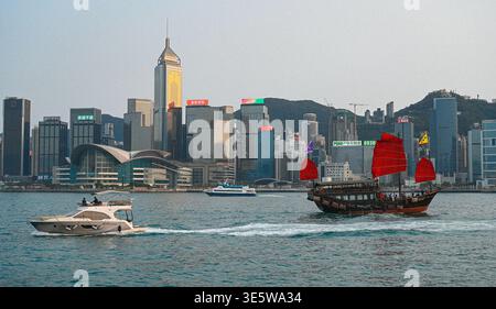 Jonque chinoise traditionnelle avec des voiles rouges naviguant à travers le port Victoria avec Hong Kong skyline en arrière-plan. Banque D'Images