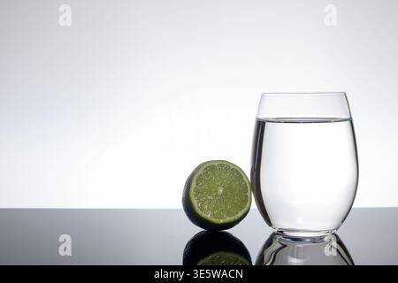 Lime tranché à côté du verre d'eau claire sur fond blanc avec espace de copie Banque D'Images