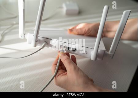 Gros plan détaillé d'une personne connectant un câble réseau à un routeur sans fil doté d'antennes. Concept de configuration Internet haut débit, su technique Banque D'Images