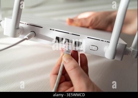 Gros plan détaillé d'une personne connectant un câble réseau à un routeur sans fil doté d'antennes. Concept de configuration Internet haut débit, su technique Banque D'Images