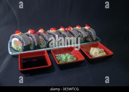 Petits pains de sushi gourmands avec riz noir, garniture de crevettes fraîches, sauce crémeuse et garniture de caviar rouge servis sur une élégante assiette en céramique - idéal pour le luxe Banque D'Images