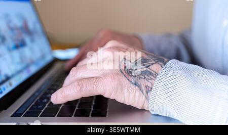 Main tatouée de la personne tapant sur un clavier d'ordinateur portable, représentant le travail et la communication numérique Banque D'Images