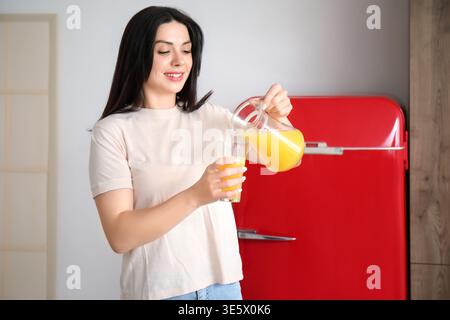 Belle femme versant du jus d'orange dans le verre dans la cuisine Banque D'Images