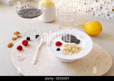 Petit déjeuner sain avec des graines de chia de yaourt et des baies fraîches dans un bol blanc sur un plateau en marbre. Le tir à grand angle comprend du citron chia pudding et des noix Banque D'Images