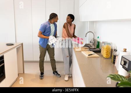 Couple laver la vaisselle dans la cuisine moderne, avec des gants en caoutchouc rose et un torchon rayé Banque D'Images