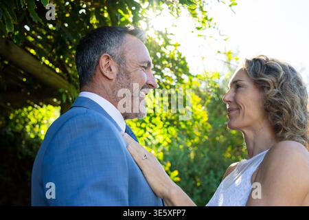 Couple en tenue formelle debout près dans le jardin sous la pergola, montrant anneau de fiançailles Banque D'Images