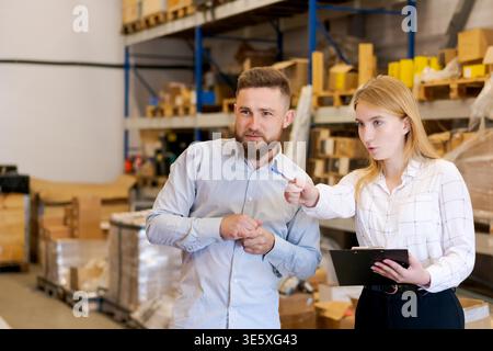 Les ouvriers d'entrepôt professionnels examinent les processus d'inventaire et de logistique. Homme et femme discutant de la gestion des stocks en utilisant le presse-papiers dans l'installation de stockage moderne. Banque D'Images