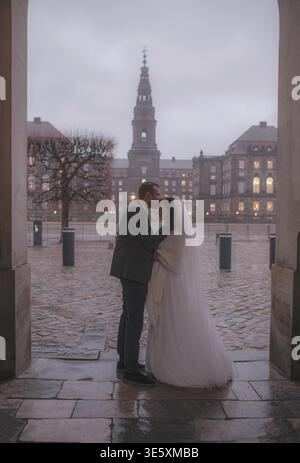 Couple de mariage romantique embrassant sous arche le jour de pluie Banque D'Images