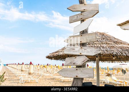 Panneau directionnel sur la plage de sable. Direction flèche en bois. Spase de copie ciel bleu. Voyages d'été. Panneau indicateur avec flèches vierges. Rangées de parasols et de chaises longues. Banque D'Images