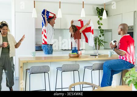 Couple acclamant un groupe diversifié portant des drapeaux américains ENG sur l'îlot de cuisine, homme en maillot rouge tenant un ballon Banque D'Images