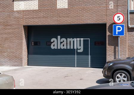 Porte de garage fermée et zone de stationnement avec panneau de limitation de vitesse sur la façade en brique du bâtiment Banque D'Images