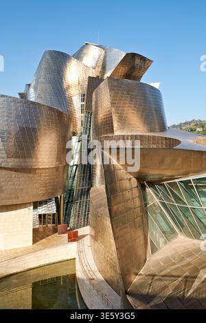 Les visiteurs admirent la structure unique du musée Guggenheim à Bilbao. Le bâtiment présente une architecture moderne contre un ciel bleu clair. Banque D'Images