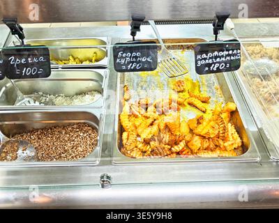 Orenburg, Russie - 22 août 2025 : différents types de nourriture, y compris les fruits de mer et le poulet, sont servis dans un comptoir de marché animé dans l'après-midi. Banque D'Images