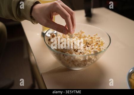Gros plan de la main masculine prenant du pop-corn du bol sur la table Banque D'Images
