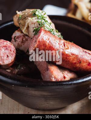 Le bol arrondi contient des saucisses salées nappées d'herbes. La surface en bois ajoute une texture rustique et chaude. Les viandes grésillantes suggèrent un plat fraîchement grillé ou rôti. Elle Banque D'Images