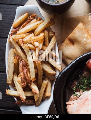 Les frites dorées reposent sur un plateau blanc. Fraîchement frit, croustillant et invitant. Servi avec saumon, herbes et pita. Repas chaleureux et réconfortant pour un dîner décontracté Banque D'Images