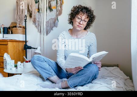 Jolie femme confiante dans son livre de lecture des années 40 sur le lit à la maison Banque D'Images