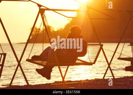 Silhouette de couple romantique sur balançoire au coucher du soleil par la mer Noire, Sotchi, Russie Banque D'Images