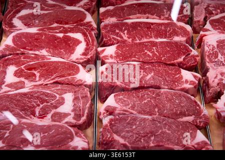 Biftecks de bœuf crus frais et striploin avec persillage exposés dans un réfrigérateur de boucherie. Viande rouge de qualité supérieure pour barbecue ou grill. Banque D'Images