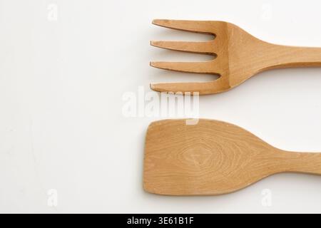 Cuillère et fourchette en bois placées sur une surface blanche, mettant en valeur la texture naturelle et le style minimaliste. Idéal pour les concepts de cuisine, respectueux de l'environnement Banque D'Images