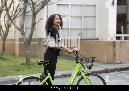 Une jeune femme confiante pose avec son vélo vert, prête à explorer la ville et à adopter un mode de vie actif et écologique Banque D'Images