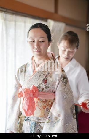 Une femme en kimono est aidée par une autre femme. La femme dans le kimono porte un arc rouge Banque D'Images
