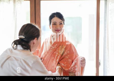 Une femme en kimono est aidée par un homme. La femme sourit et l'homme porte une chemise blanche Banque D'Images