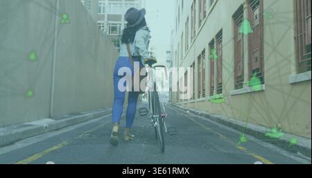 Femme asiatique marchant avec chapeau à bord, pantalon bleu poussant le vélo dans l'allée urbaine avec des revêtements AR Banque D'Images
