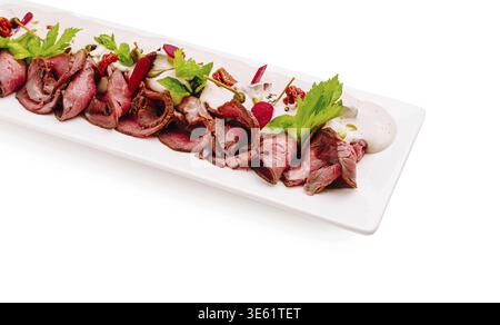 Nourriture, Un plat de rôti de bœuf magnifiquement arrangé avec de fines tranches de bœuf garnies d'herbes fraîches, arrosées de sauce et complétées par du col Banque D'Images