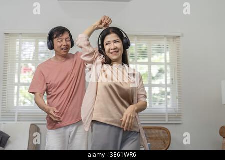 Un couple plus âgé partage une danse joyeuse ensemble, portant des écouteurs et profitant de la musique dans leur maison lumineuse et accueillante Banque D'Images