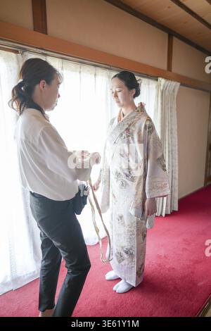 Une femme en kimono est aidée par une autre femme. La femme dans le kimono porte une chemise blanche et un pantalon noir Banque D'Images