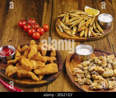 Nourriture, assortiment de fruits de mer frits sont présentés sur des assiettes en bois, avec de petits poissons, des calamars et des crustacés. Tomates cerises fraîches et tranches de citron comp Banque D'Images