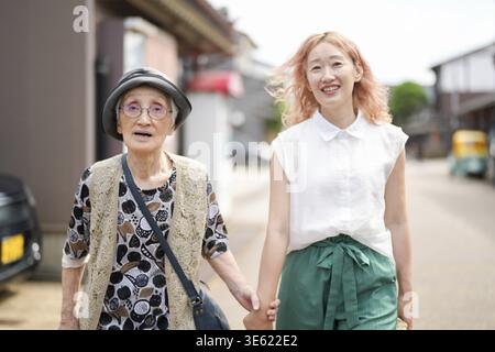 Deux femmes marchant dans une rue, l'une d'elles porte un chapeau et des lunettes. L'autre femme porte une chemise blanche et un pantalon vert Banque D'Images