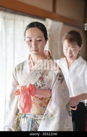 Une femme en kimono est aidée par une autre femme. La femme dans le kimono porte un arc rose Banque D'Images
