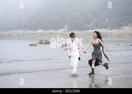 En juin 2025, un homme et une femme coréens dans la cinquantaine courent à pleine vitesse le long du littoral accidenté rempli de rochers déchiquetés et de crashs Banque D'Images