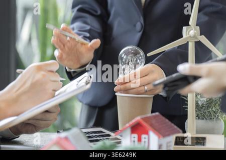 Les professionnels des affaires collaborent sur des solutions d'énergie durable, en présentant une ampoule dans une tasse, mettant l'accent sur des approches innovantes de l'énergie Banque D'Images