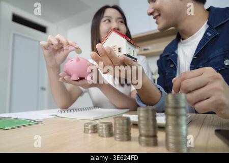 Un jeune couple discute de leur avenir financier, tenant une tirelire et un modèle de maison, symbolisant leurs objectifs d'investissement Banque D'Images