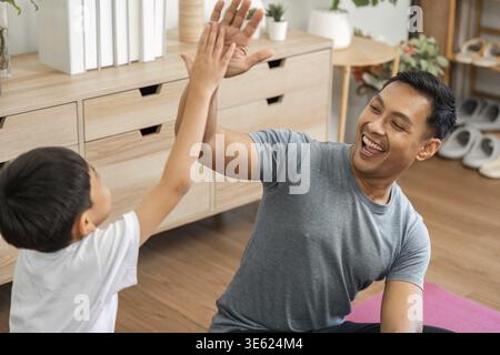 Un père et un fils joyeux se livrent à des activités sportives ludiques à la maison, favorisant la forme physique, le rire et de solides liens familiaux Banque D'Images