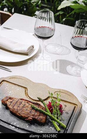 Nourriture, Un succulent steak grillé est présenté aux côtés des asperges et des tomates cerises sur une assiette élégante. Deux verres de vin rouge complètent l'élégant Banque D'Images